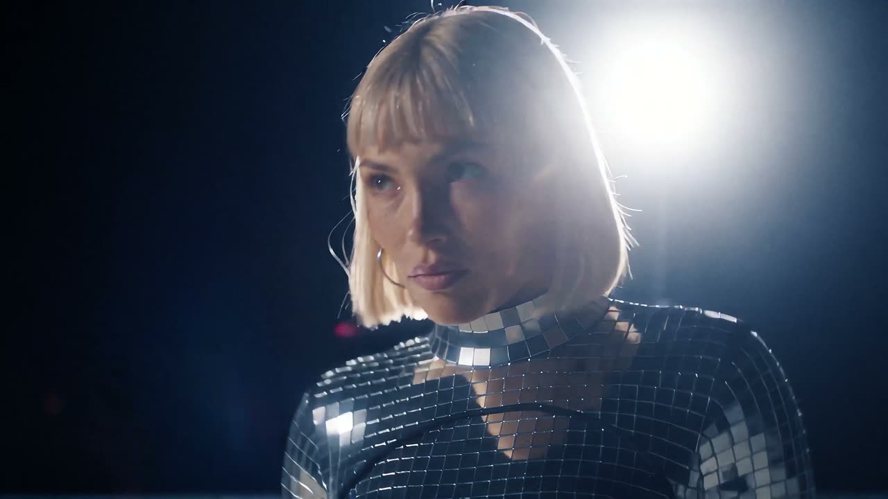 Vera Noctis under a stage light in a mirrored top, from the Afterglow music video