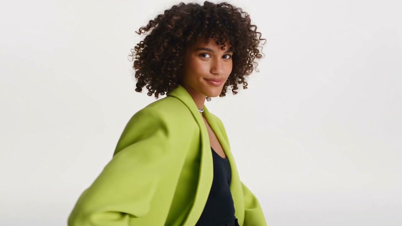 A pop performer in a lime jacket and pink boots against a bright studio backdrop.