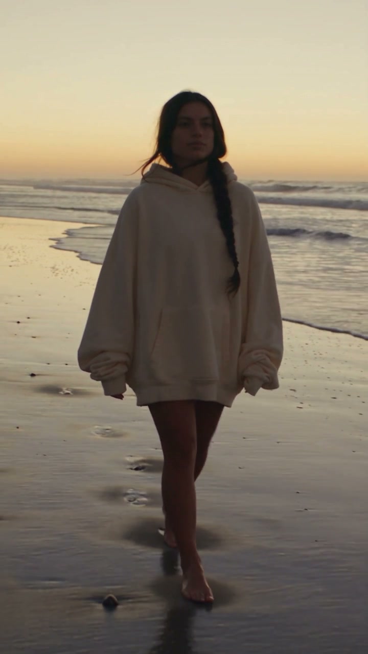 An alt-pop portrait moves from the beach at sunrise to a warm pink evening sky.