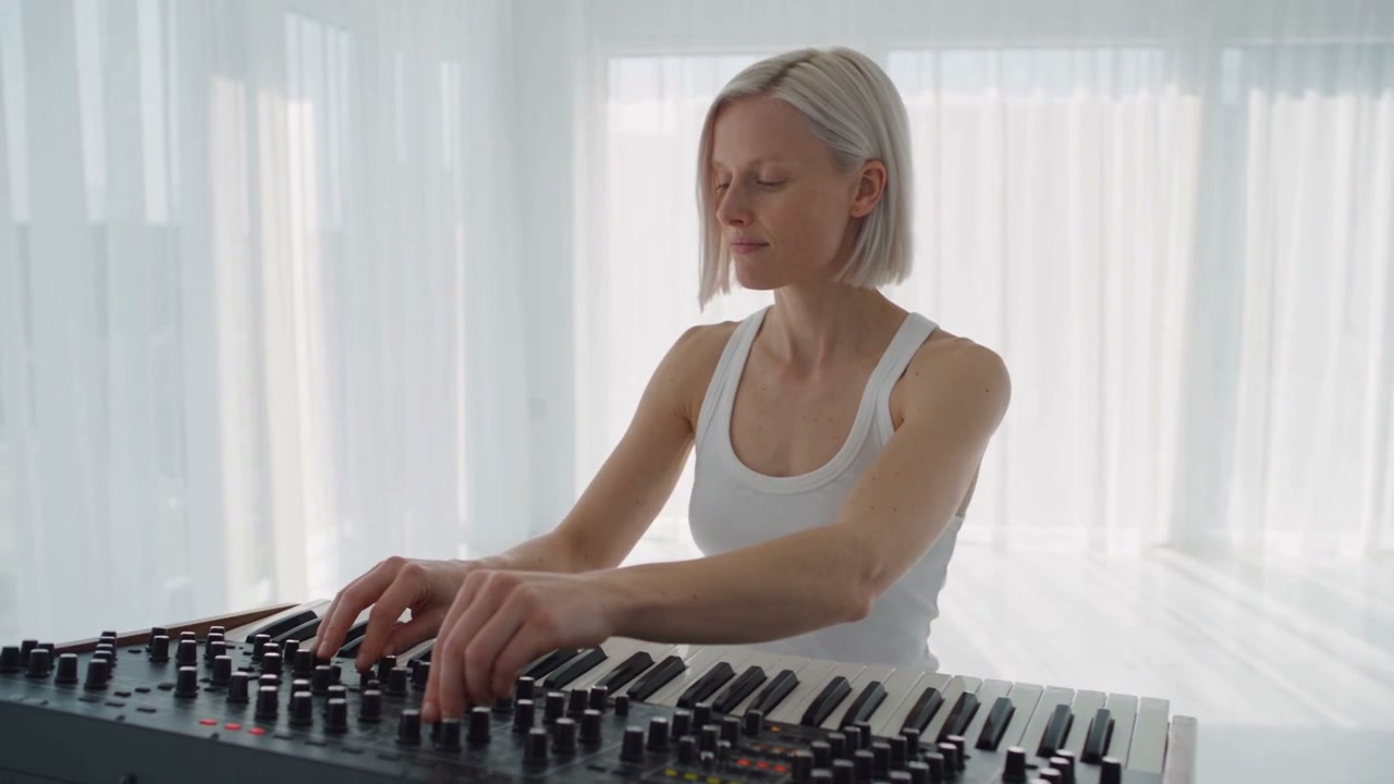 An electronic artist at a mixing desk in a bright loft, framed by colored cables.