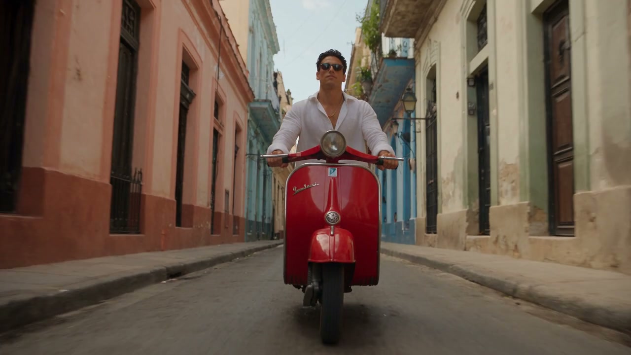A Latin-pop scene moves from a rooftop pool to a red scooter on a sunlit street.